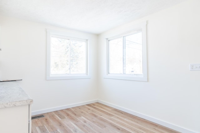 unfurnished room with baseboards, a textured ceiling, visible vents, and light wood-style floors