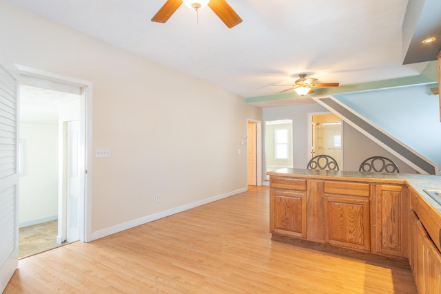 kitchen featuring a ceiling fan, brown cabinets, light wood-style flooring, and baseboards