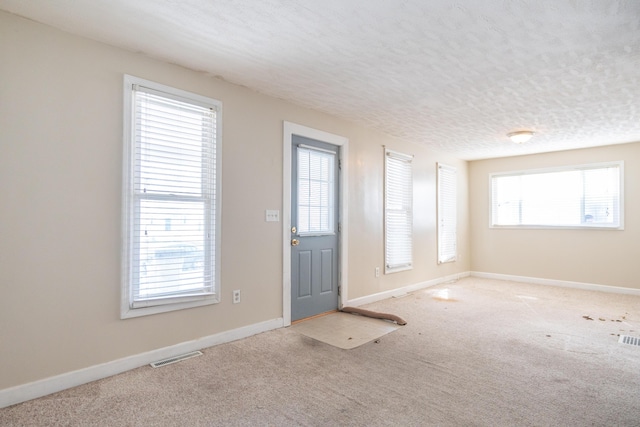 entryway with baseboards, visible vents, a textured ceiling, and light colored carpet