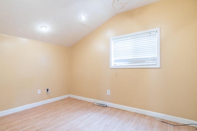 spare room featuring lofted ceiling, light wood-type flooring, visible vents, and baseboards