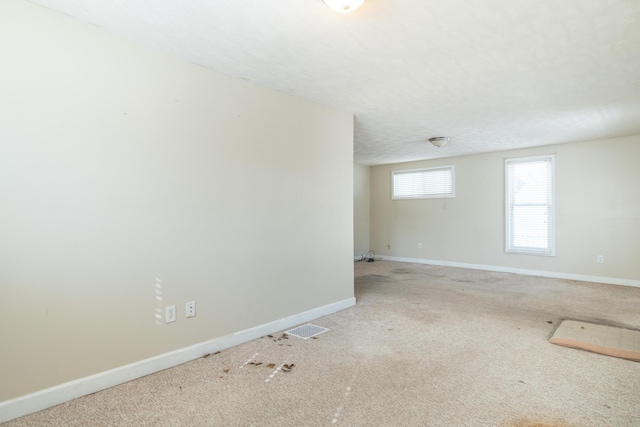 carpeted empty room featuring a textured ceiling, visible vents, and baseboards