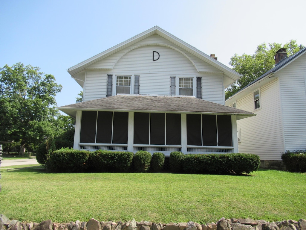 view of front of property featuring roof with shingles, a front lawn, and a sunroom