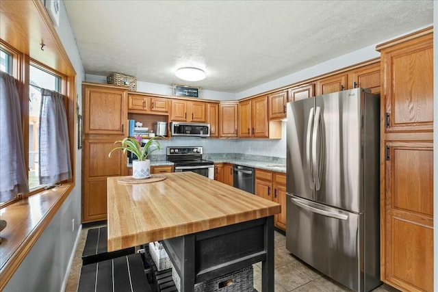 kitchen featuring appliances with stainless steel finishes, light tile patterned flooring, brown cabinets, and a healthy amount of sunlight