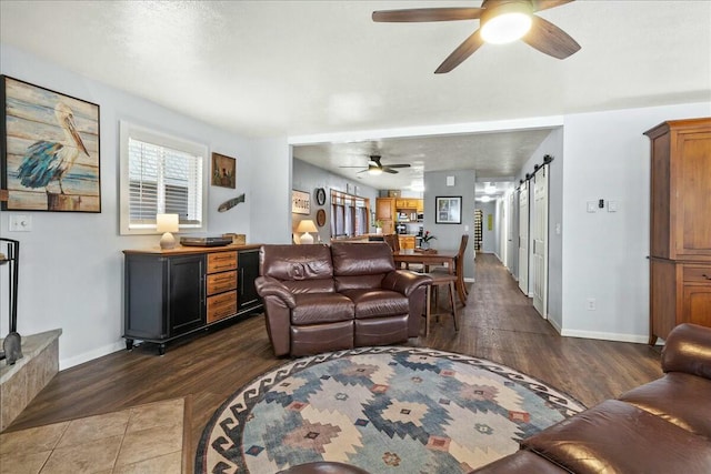 living area featuring a barn door, dark wood-style flooring, a ceiling fan, and baseboards