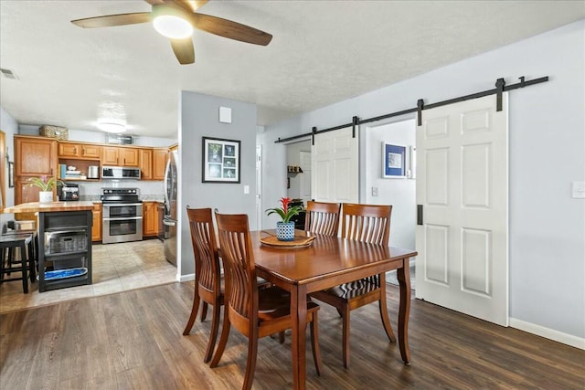 dining room with ceiling fan, a barn door, light wood-style flooring, and baseboards