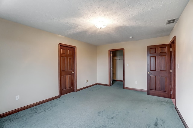 unfurnished bedroom with a spacious closet, light colored carpet, a textured ceiling, and a closet