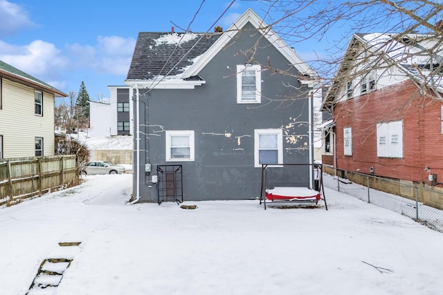 snow covered rear of property featuring fence and stucco siding