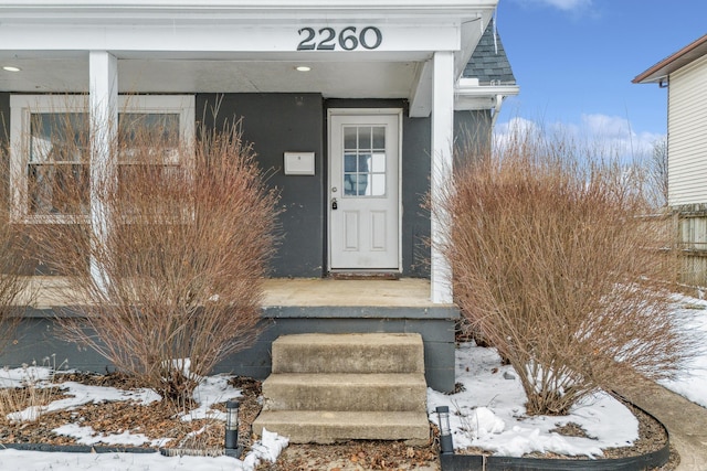 snow covered property entrance with roof with shingles