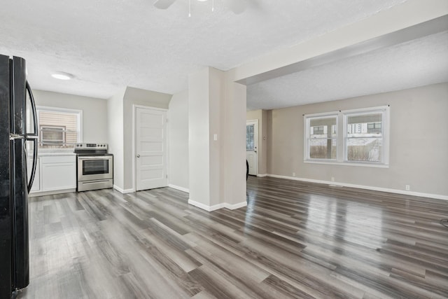 kitchen featuring stainless steel electric stove, freestanding refrigerator, white cabinetry, wood finished floors, and baseboards