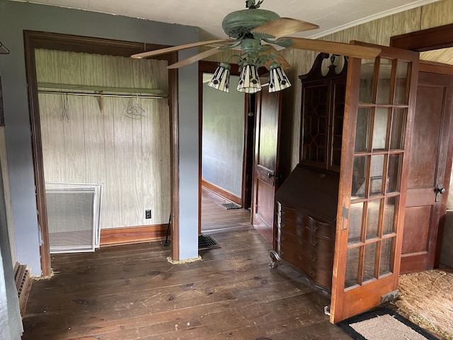 unfurnished dining area with ceiling fan, wood walls, and dark wood-type flooring