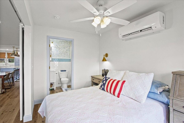 bedroom featuring ceiling fan, connected bathroom, wood finished floors, a wall mounted air conditioner, and baseboards