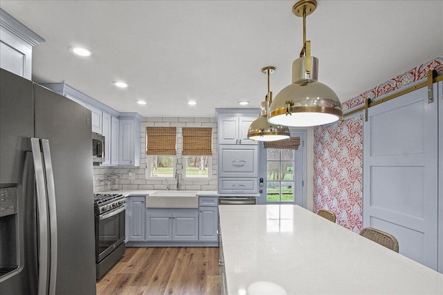 kitchen with light countertops, gray cabinetry, a barn door, appliances with stainless steel finishes, and a sink