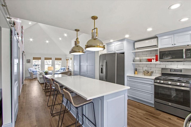 kitchen featuring pendant lighting, a breakfast bar area, light countertops, appliances with stainless steel finishes, and an AC wall unit