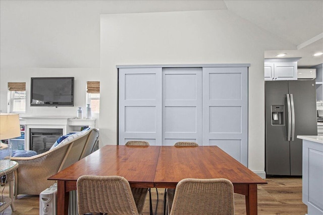 dining room with light wood-type flooring, a glass covered fireplace, and vaulted ceiling