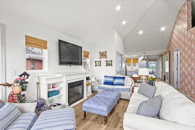 living area featuring a healthy amount of sunlight, light wood finished floors, high vaulted ceiling, and a glass covered fireplace