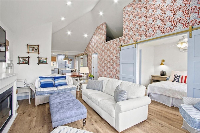 living room with high vaulted ceiling, a barn door, light wood-style flooring, and wallpapered walls