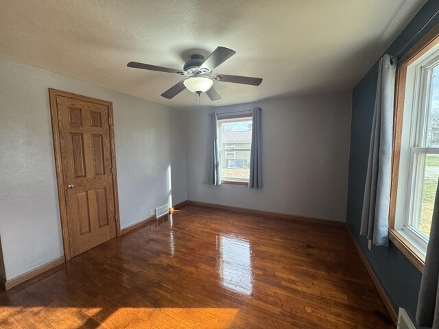 empty room featuring a ceiling fan, visible vents, baseboards, and wood finished floors