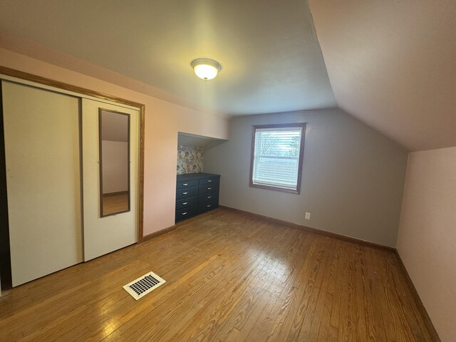 unfurnished bedroom featuring baseboards, light wood-style flooring, visible vents, and vaulted ceiling