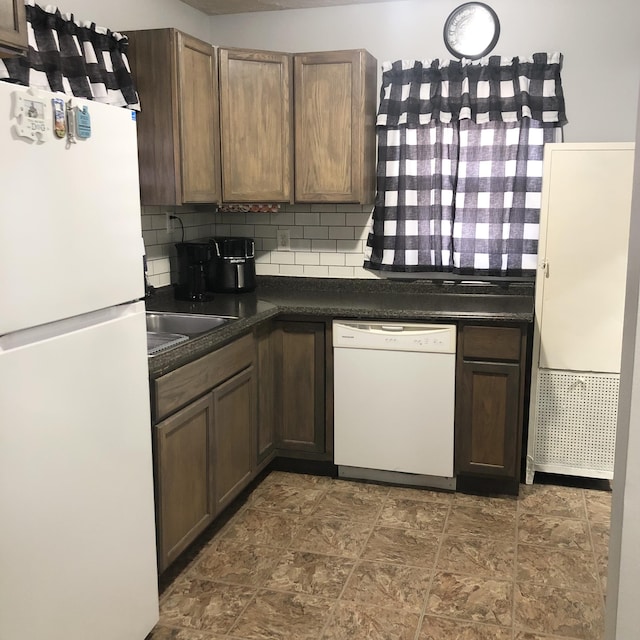 kitchen with dark countertops, white appliances, a sink, and decorative backsplash