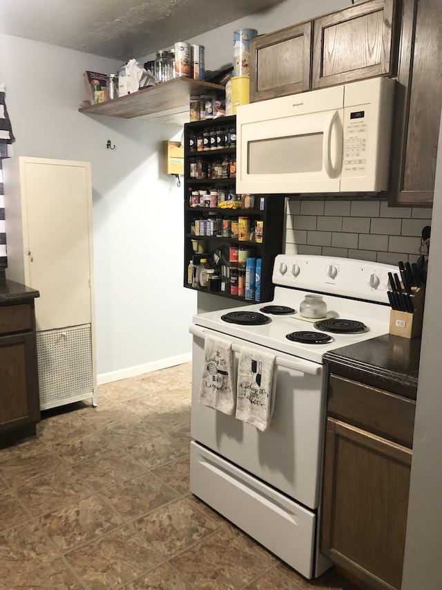 kitchen with dark brown cabinetry, white appliances, open shelves, tasteful backsplash, and dark countertops