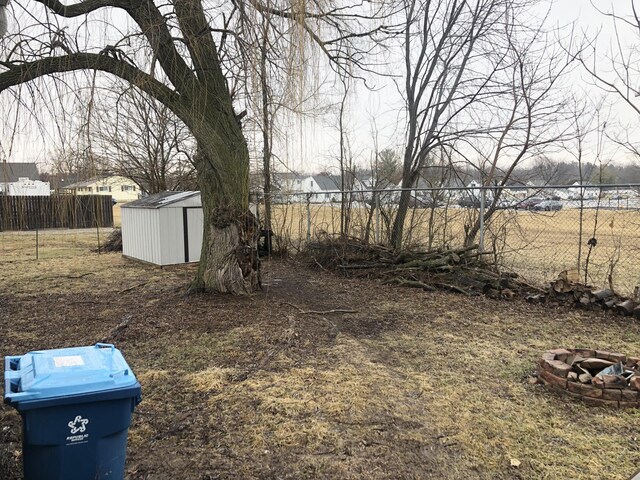 view of yard featuring a storage shed, fence, a fire pit, and an outdoor structure