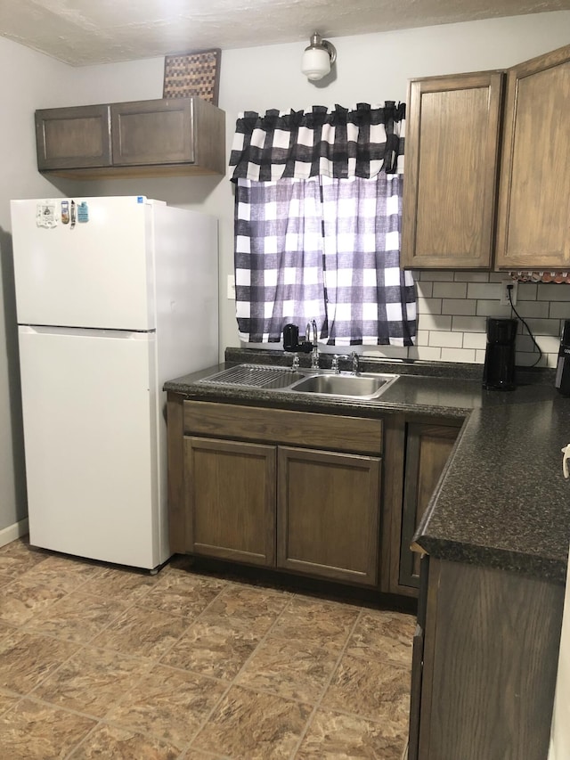 kitchen featuring freestanding refrigerator, backsplash, a sink, and dark countertops