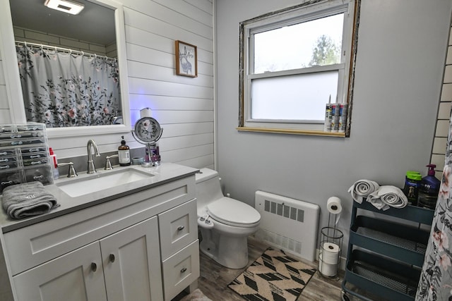 bathroom featuring toilet, wood walls, vanity, radiator, and hardwood / wood-style flooring