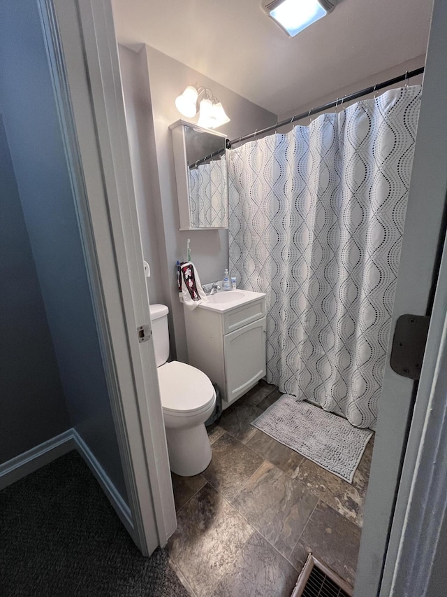 full bath with stone finish flooring, vanity, and toilet