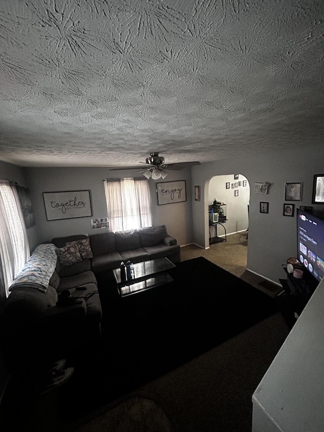 carpeted living area with a ceiling fan, arched walkways, and a textured ceiling