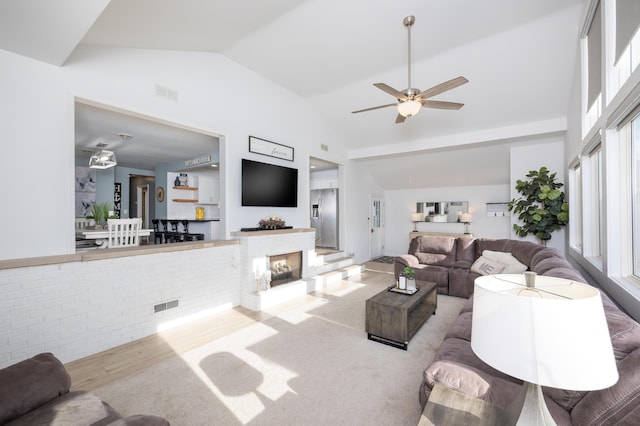 living area featuring visible vents, wood finished floors, high vaulted ceiling, and a fireplace with raised hearth