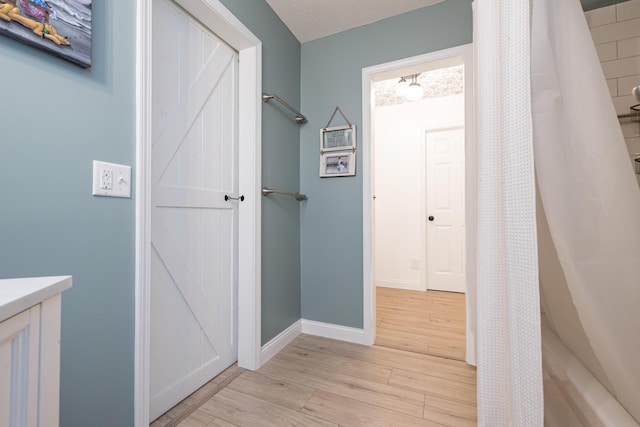 full bathroom with a textured ceiling, a shower with shower curtain, baseboards, and wood finished floors