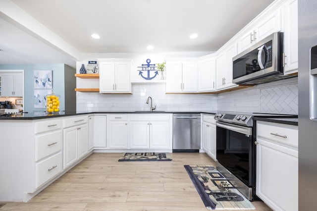 kitchen with light wood finished floors, open shelves, white cabinets, appliances with stainless steel finishes, and dark countertops