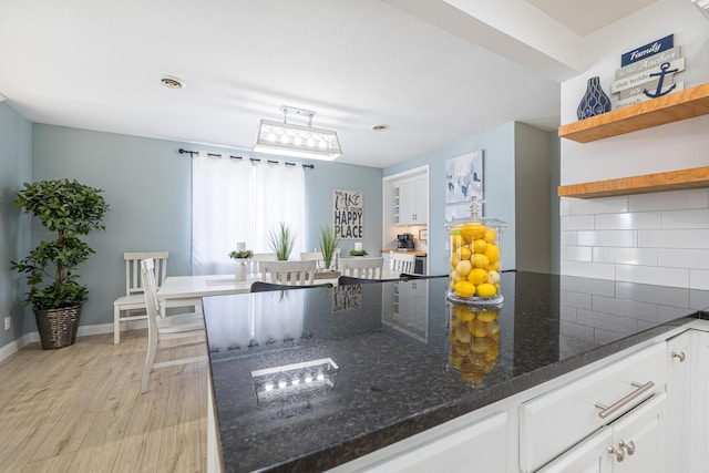 kitchen featuring decorative backsplash, dark stone countertops, light wood-style flooring, white cabinets, and open shelves