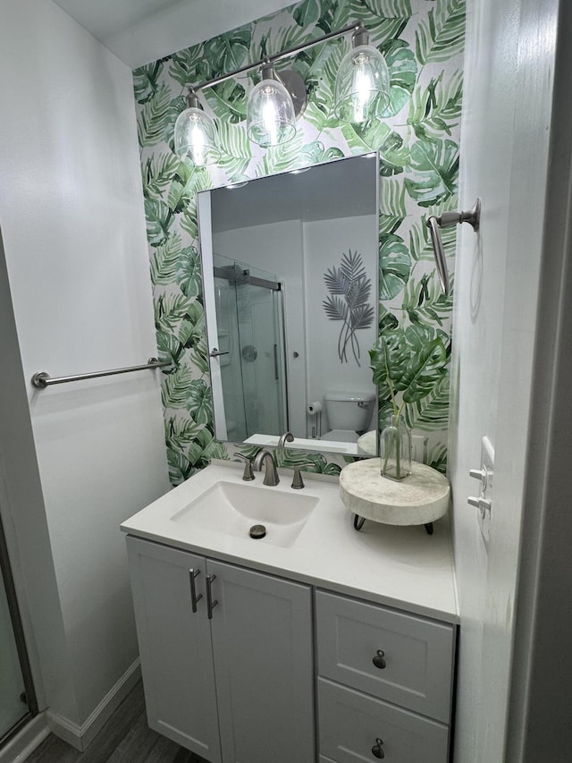 bathroom featuring vanity, baseboards, wallpapered walls, a shower stall, and toilet