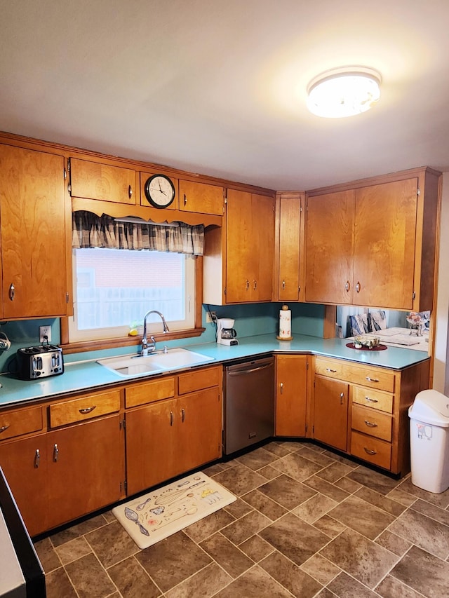 kitchen featuring stone finish floor, brown cabinetry, a sink, and dishwasher