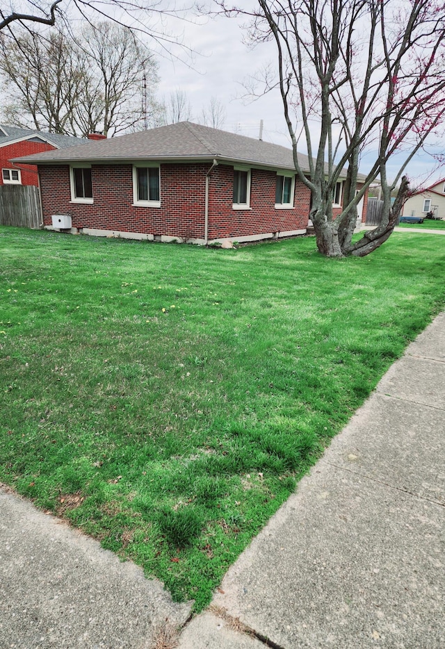 exterior space with a lawn, a shingled roof, and brick siding