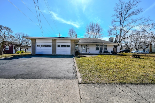 ranch-style home featuring driveway, a chimney, an attached garage, covered porch, and a front yard