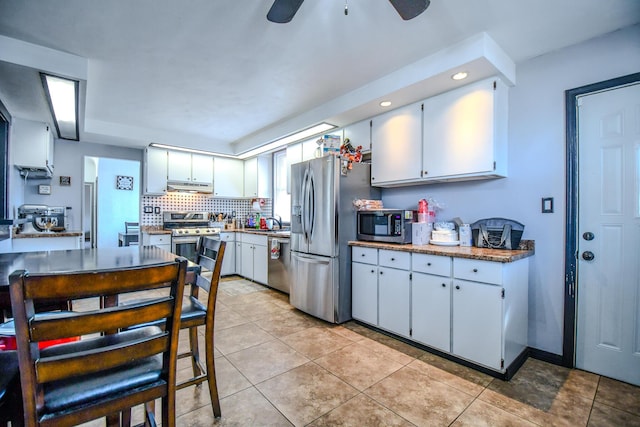 kitchen featuring light tile patterned floors, tasteful backsplash, white cabinets, appliances with stainless steel finishes, and range hood