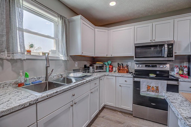 1313 Arrowhead, Piqua, OH 45356 - kitchen featuring appliances with stainless steel finishes, white cabinetry, light countertops, light wood-type flooring, and a textured ceiling