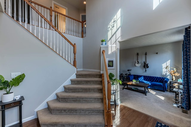 stairway featuring a high ceiling, wood finished floors, and baseboards