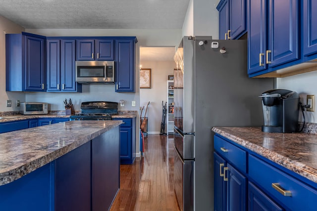 kitchen with blue cabinetry, stainless steel microwave, dark countertops, dark wood finished floors, and black gas range oven