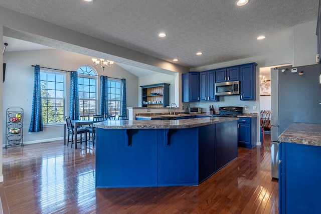 kitchen with blue cabinets, a peninsula, a sink, appliances with stainless steel finishes, and a kitchen bar