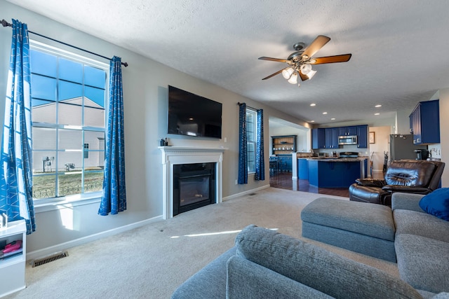 living area featuring carpet floors, visible vents, a glass covered fireplace, a textured ceiling, and baseboards