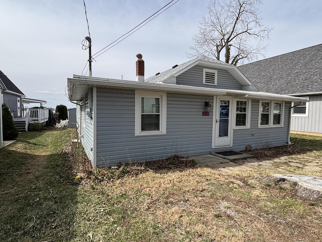 rear view of property featuring a chimney and a yard