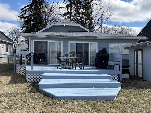 rear view of house with a yard, a shingled roof, a deck, and fence