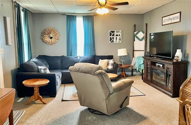 living room featuring carpet, wooden walls, a drop ceiling, and ceiling fan