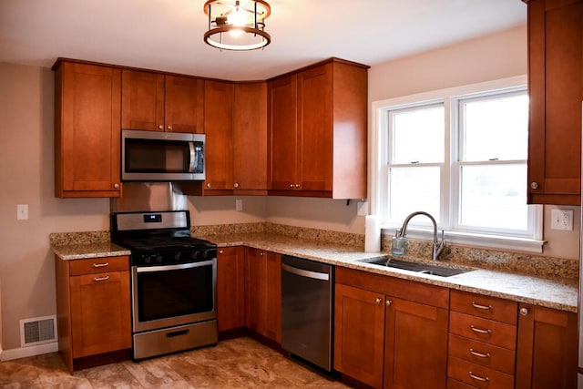 kitchen featuring brown cabinetry, visible vents, stainless steel appliances, and a sink