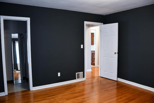 empty room with wood finished floors, visible vents, and baseboards