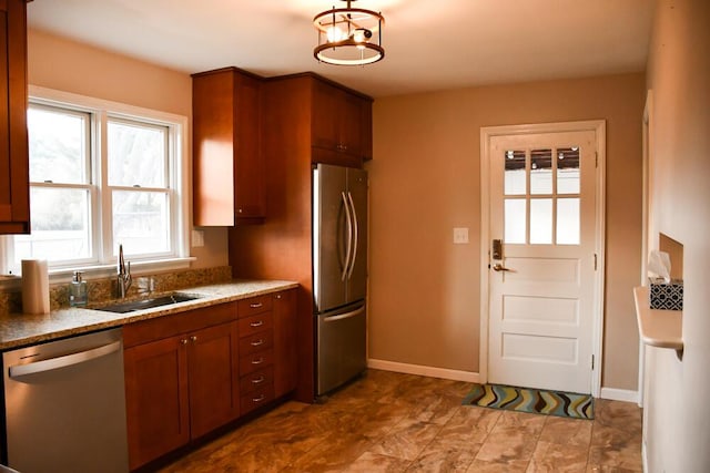 kitchen with baseboards, appliances with stainless steel finishes, brown cabinets, and a sink