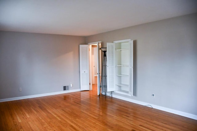 unfurnished bedroom featuring wood finished floors, visible vents, and baseboards